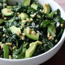 A bowl of kale salad with avocado and pine nuts