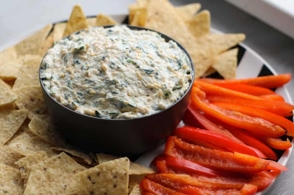 Spinach dip in a bowl with chips and peppers