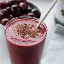 Smoothie in a glass with a straw and a bowl of cherries behind it