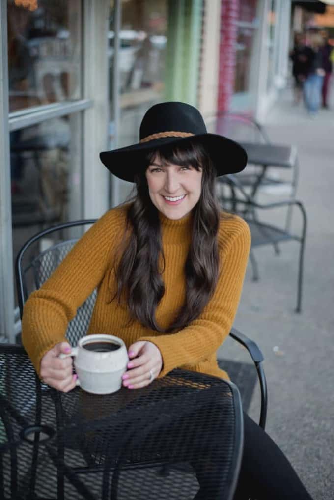 A person sitting at a table with a cup of coffee and a hat