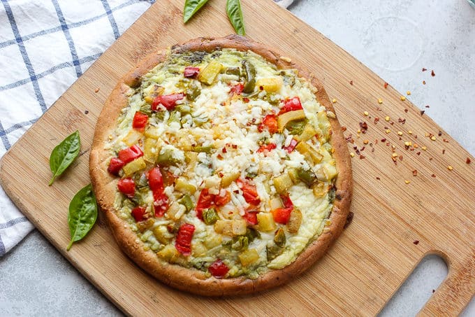 A pizza sitting on top of a wooden cutting board, with Cheese and Pesto pizza