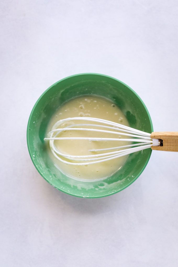 A green bowl on a table, with Spoon and Whisk with glaze